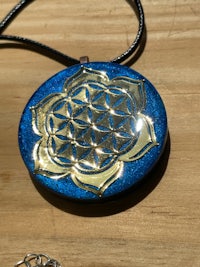 a blue and gold flower of life pendant on a wooden table