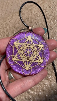 a person holding a purple and gold shamanic pendant