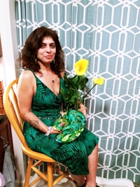 a woman in a green dress sitting on a chair holding flowers