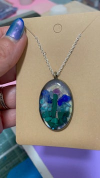 a person is holding a necklace with a painting on it