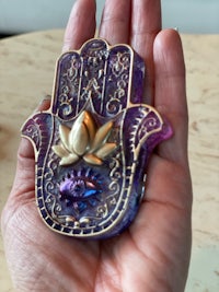 a person holding a purple hamsa in their hand